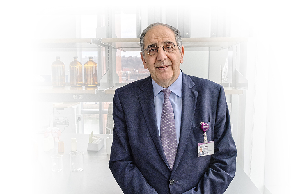 Dr. Jose-Alain Sahel dressed in a suit stands in front of laboratory equipment. 